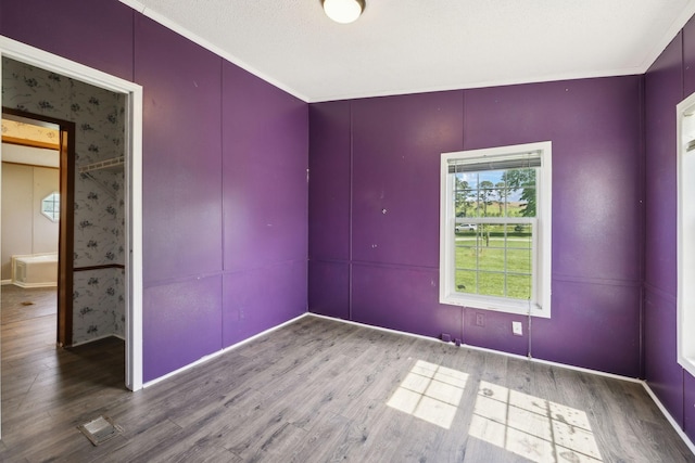 empty room with wood finished floors, a decorative wall, crown molding, and baseboards