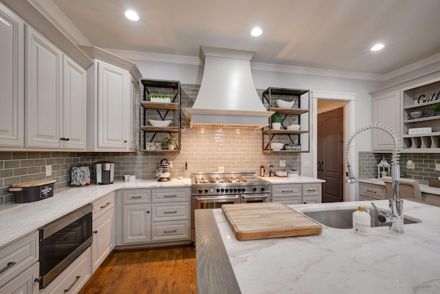kitchen with premium range hood, open shelves, appliances with stainless steel finishes, a sink, and backsplash