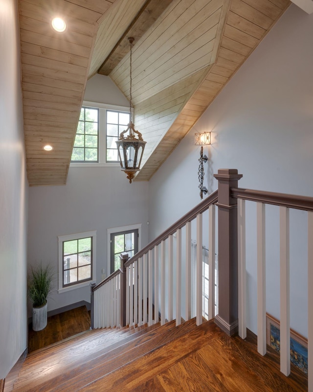 stairs with wooden ceiling, wood finished floors, plenty of natural light, beam ceiling, and a chandelier