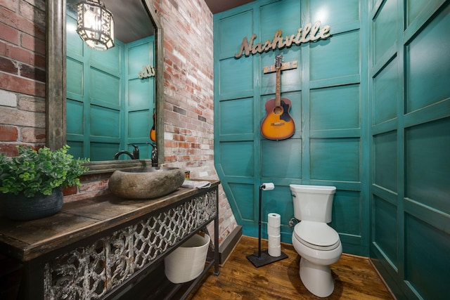 bathroom with toilet, wood finished floors, brick wall, vanity, and a decorative wall