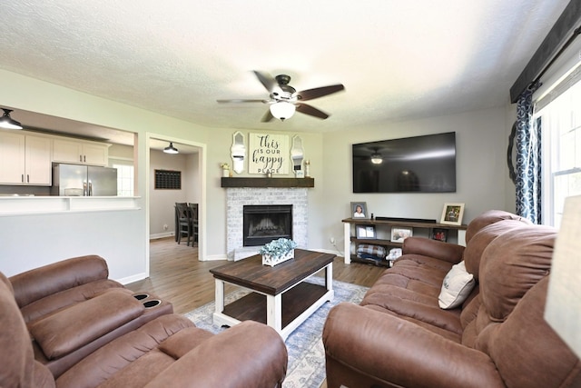 living area featuring a ceiling fan, wood finished floors, baseboards, and a fireplace with raised hearth