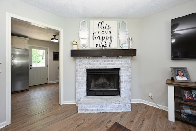living area featuring a textured ceiling, wood finished floors, a brick fireplace, and baseboards