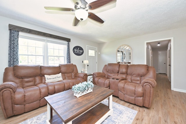 living room featuring ceiling fan, light wood finished floors, a textured ceiling, and baseboards