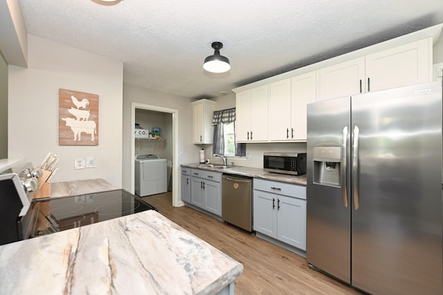 kitchen featuring appliances with stainless steel finishes, a sink, light wood finished floors, a textured ceiling, and white cabinets