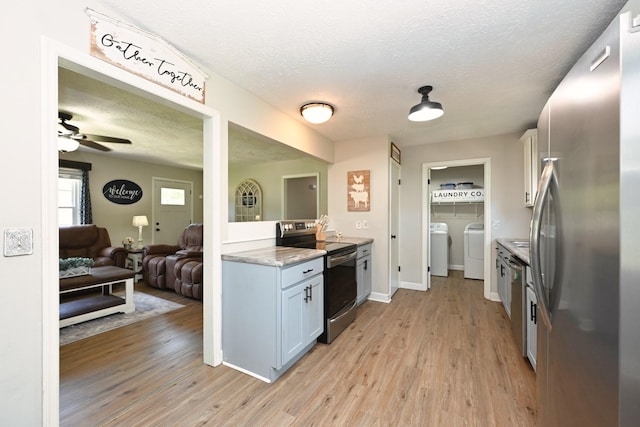 kitchen featuring appliances with stainless steel finishes, washer and clothes dryer, light wood-type flooring, a textured ceiling, and open floor plan