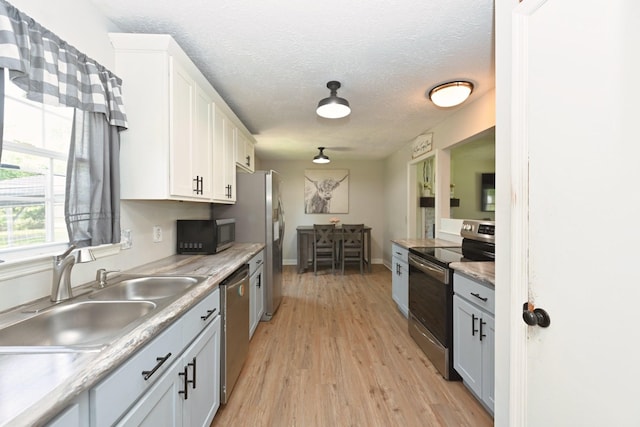 kitchen featuring appliances with stainless steel finishes, a sink, white cabinetry, light wood-type flooring, and a textured ceiling