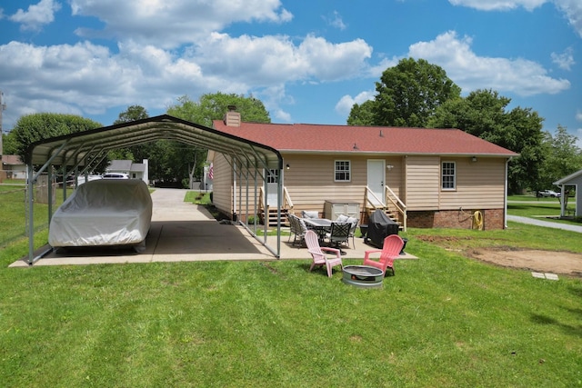 rear view of property featuring a carport, entry steps, a lawn, a chimney, and a fire pit