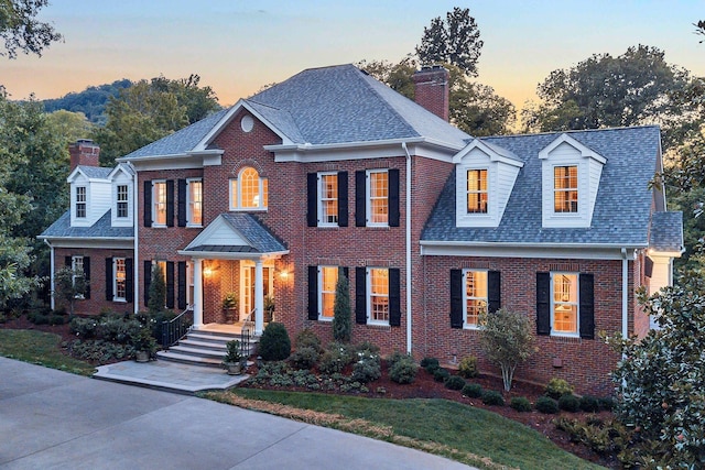 colonial-style house featuring brick siding, a shingled roof, and a chimney