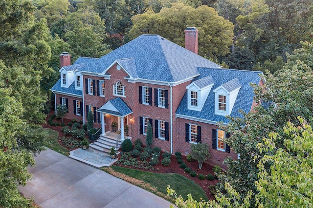colonial home featuring a chimney, brick siding, and a view of trees