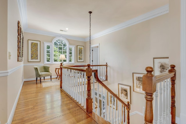 corridor with an upstairs landing, light wood-type flooring, ornamental molding, and baseboards