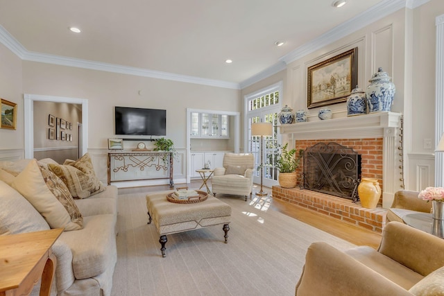 living room featuring ornamental molding, a decorative wall, a brick fireplace, a wainscoted wall, and recessed lighting