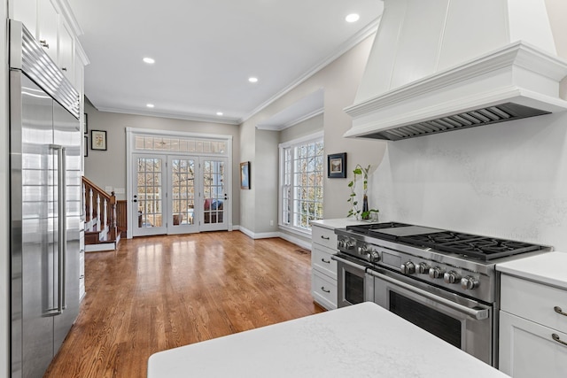 kitchen featuring high end appliances, custom range hood, light countertops, crown molding, and white cabinets