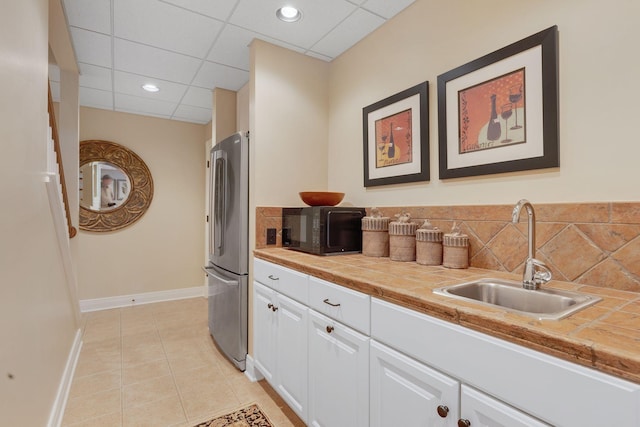 kitchen featuring black microwave, a sink, freestanding refrigerator, white cabinetry, and baseboards