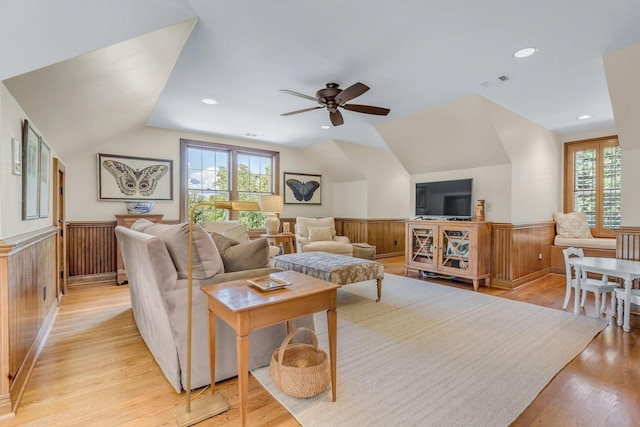 living area featuring a wainscoted wall, plenty of natural light, lofted ceiling, light wood-style floors, and ceiling fan
