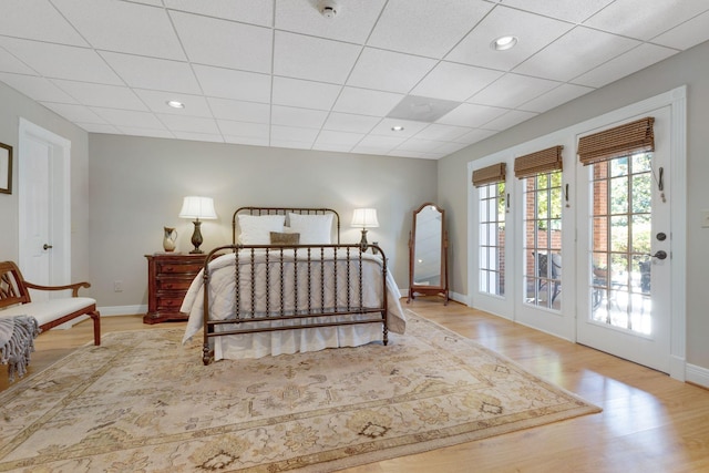 bedroom with baseboards, wood finished floors, access to exterior, a drop ceiling, and recessed lighting