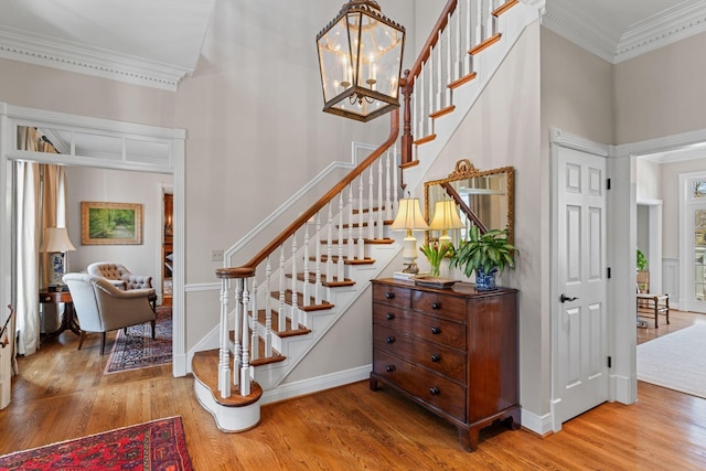 stairway featuring crown molding, wood finished floors, baseboards, and a chandelier