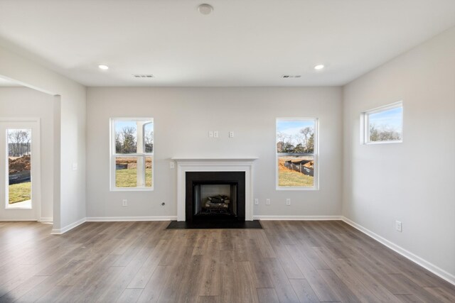 unfurnished living room featuring dark wood-style flooring, plenty of natural light, a fireplace with flush hearth, and recessed lighting