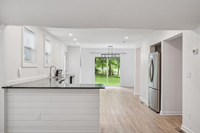 kitchen featuring freestanding refrigerator, a sink, light wood-style floors, baseboards, and recessed lighting
