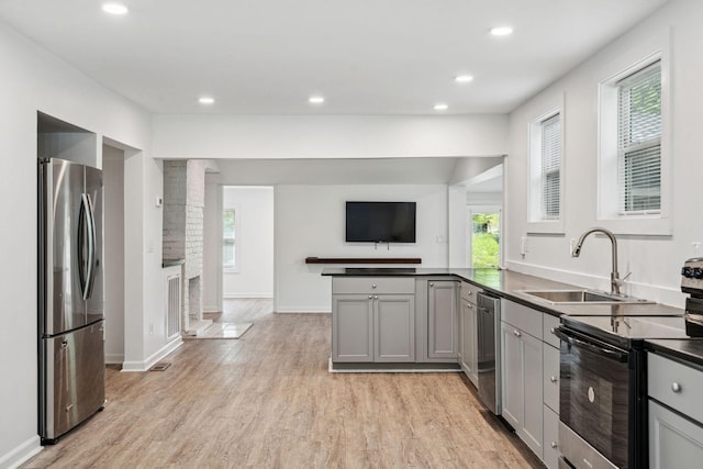 kitchen featuring appliances with stainless steel finishes, a sink, gray cabinets, dark countertops, and light wood finished floors