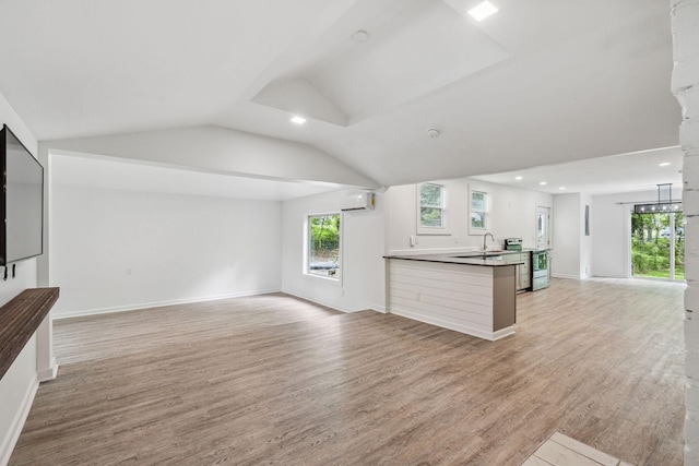 unfurnished living room with a wall unit AC, light wood-type flooring, a sink, vaulted ceiling, and baseboards