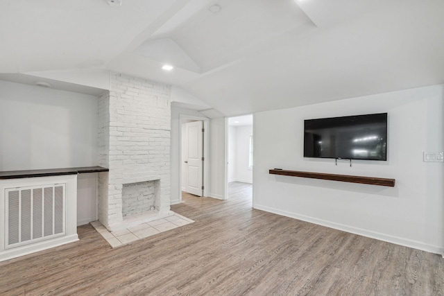 unfurnished living room with lofted ceiling, wood finished floors, baseboards, and a brick fireplace