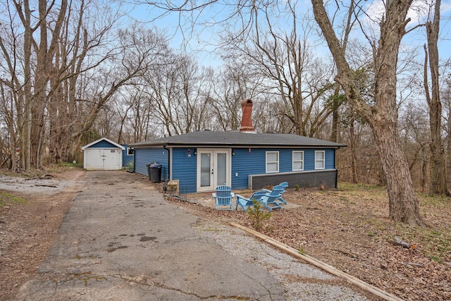 view of front of home with driveway, a detached garage, a storage shed, an outdoor structure, and a chimney