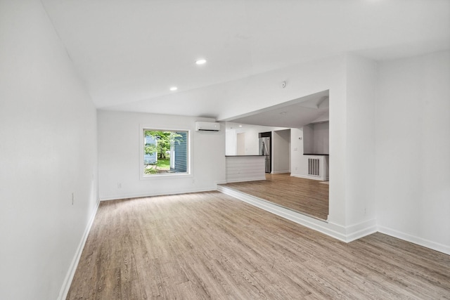 unfurnished living room featuring light wood-type flooring, baseboards, a wall mounted AC, recessed lighting, and vaulted ceiling