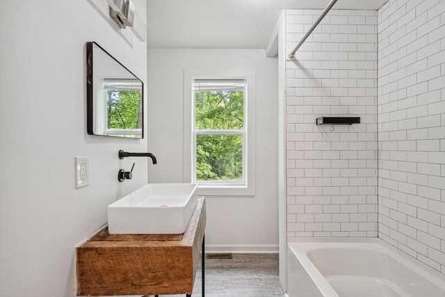 full bath with a sink, wood finished floors, shower / washtub combination, and baseboards