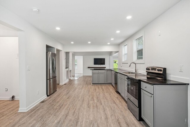 kitchen with stainless steel appliances, a sink, gray cabinets, light wood-style flooring, and dark countertops