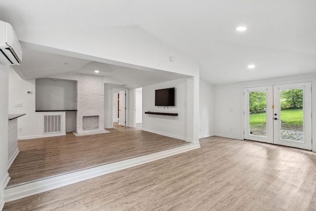 unfurnished living room featuring lofted ceiling, a wall unit AC, wood finished floors, baseboards, and a stone fireplace