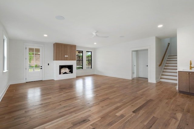 unfurnished living room featuring stairs, ceiling fan, light wood-style flooring, a fireplace, and baseboards