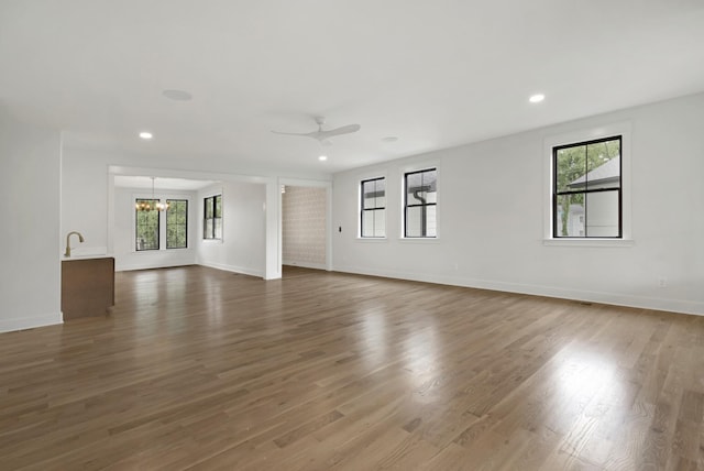 unfurnished living room with plenty of natural light, ceiling fan, wood finished floors, a chandelier, and recessed lighting
