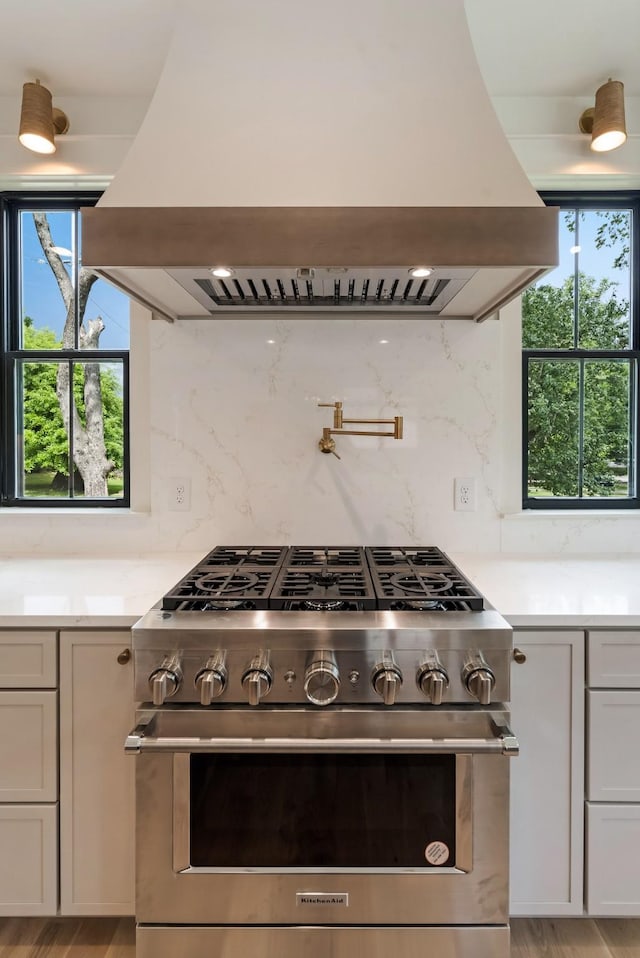 kitchen featuring high end stainless steel range, island exhaust hood, light countertops, and tasteful backsplash