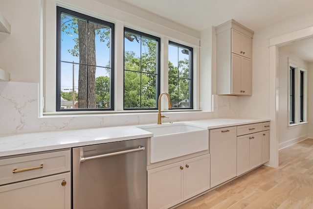 kitchen featuring stainless steel dishwasher, a sink, light wood finished floors, light stone countertops, and tasteful backsplash