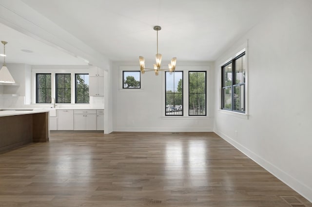unfurnished dining area featuring a chandelier, baseboards, and wood finished floors