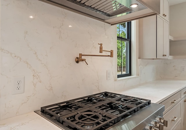 kitchen with tasteful backsplash, white cabinets, light stone counters, and stovetop