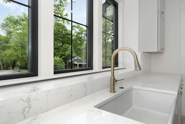 kitchen view of a sink, light stone counters, and white cabinets