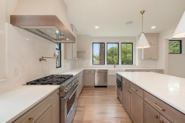kitchen featuring appliances with stainless steel finishes, island exhaust hood, a sink, light wood-style flooring, and decorative backsplash