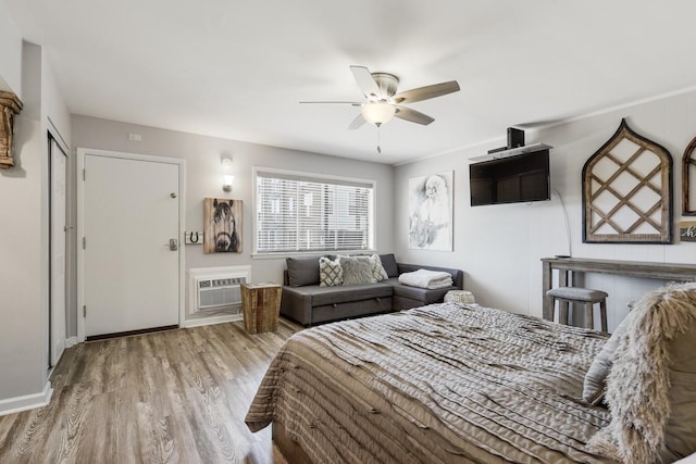 bedroom featuring wood finished floors, ceiling fan, baseboards, and a wall mounted air conditioner