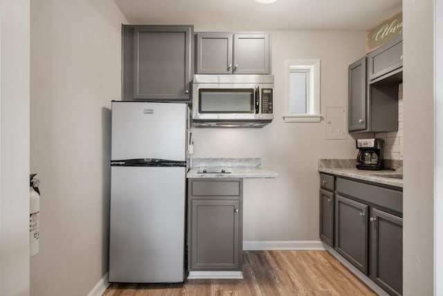 kitchen with stainless steel appliances, gray cabinetry, light wood-style floors, and light countertops