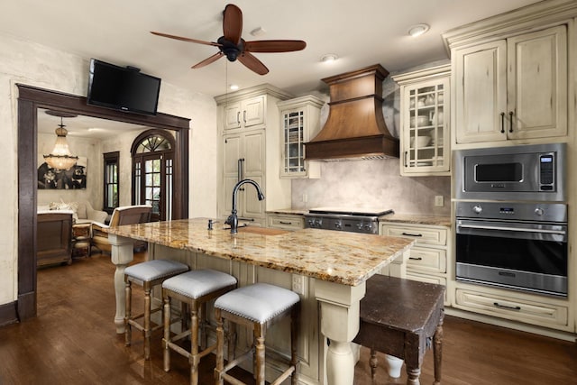 kitchen featuring stainless steel appliances, custom range hood, cream cabinets, dark wood-style floors, and a sink