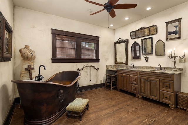 bathroom featuring ceiling fan, wood finished floors, double vanity, a freestanding bath, and recessed lighting