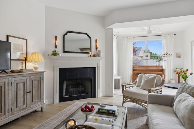 living room with wood finished floors, a tiled fireplace, a ceiling fan, and baseboards