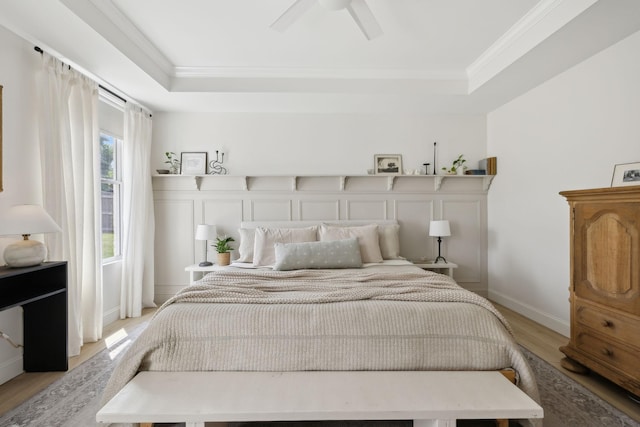 bedroom with light wood finished floors, a tray ceiling, ornamental molding, baseboards, and ceiling fan
