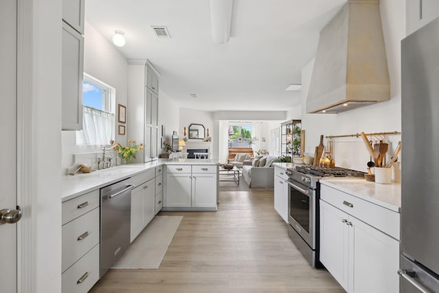kitchen with stainless steel appliances, custom range hood, open floor plan, light wood finished floors, and a peninsula
