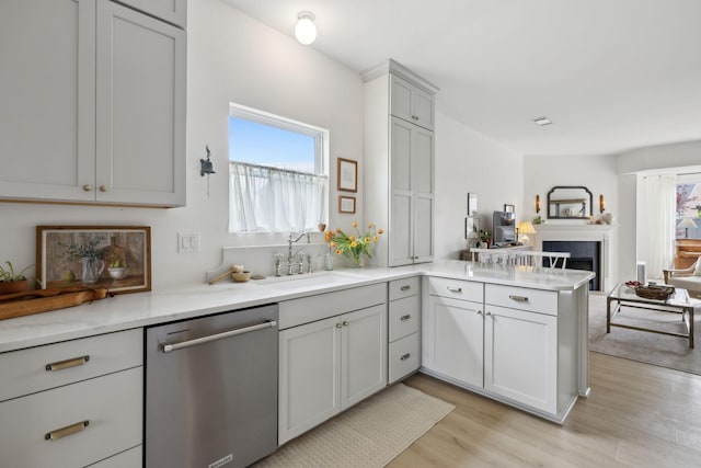 kitchen with dishwasher, a sink, open floor plan, a peninsula, and light wood-type flooring
