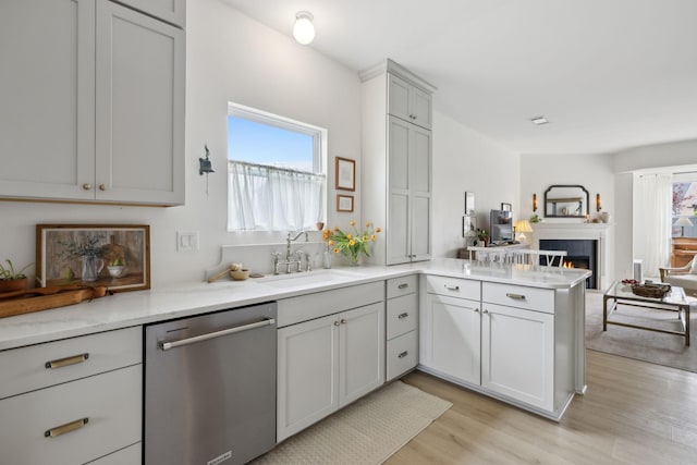 kitchen featuring dishwasher, a sink, open floor plan, a peninsula, and light wood-style flooring