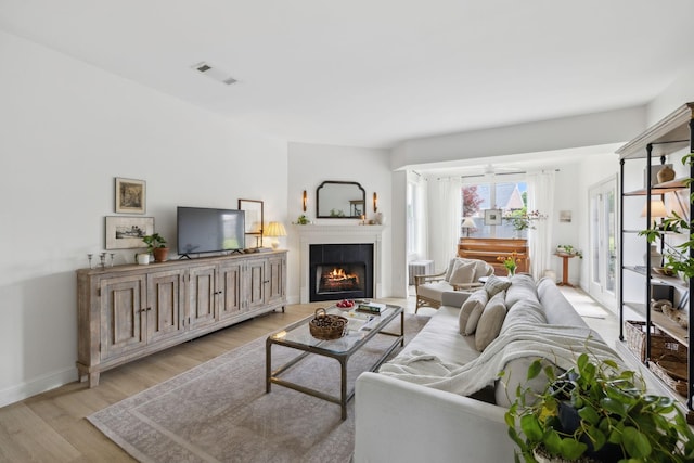living area with light wood-type flooring, a warm lit fireplace, and baseboards