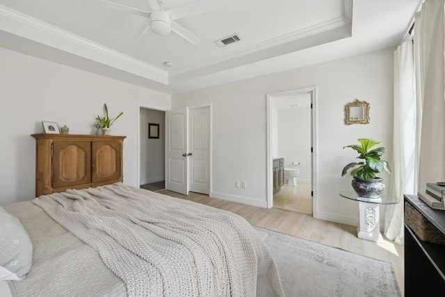bedroom featuring light wood-style floors, a tray ceiling, crown molding, connected bathroom, and baseboards