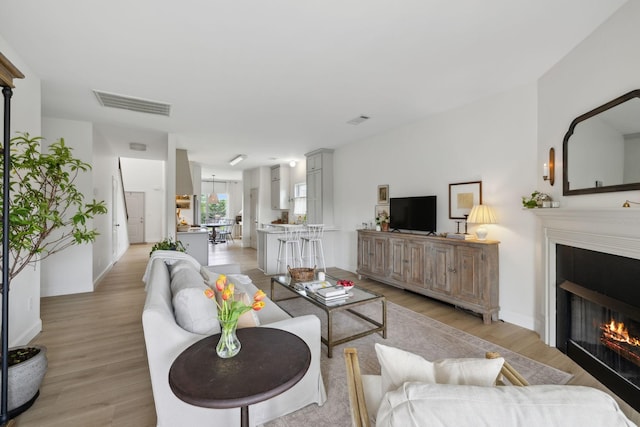 living area featuring light wood finished floors, a glass covered fireplace, and baseboards